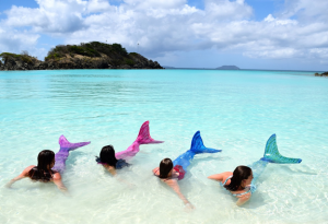 girls with costume mermaid fins on shore