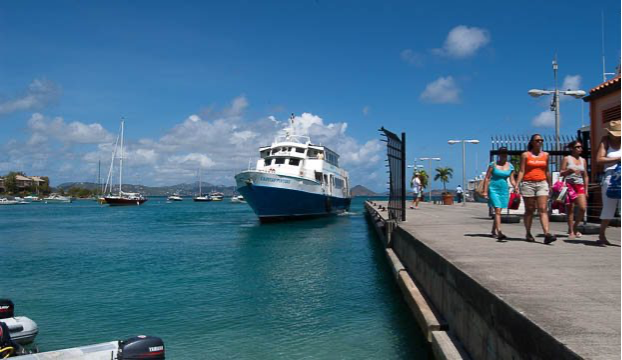 A ferry approaches a dock in St. Thomas as people walk along the waterfront on a sunny day